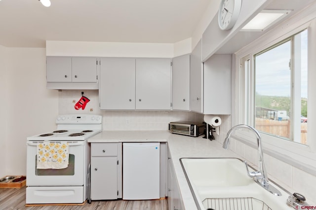 kitchen featuring white appliances, a toaster, a sink, light countertops, and backsplash