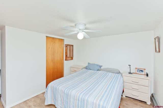 bedroom featuring light wood finished floors, baseboard heating, and baseboards