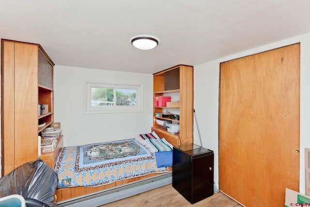 bedroom featuring a baseboard heating unit, a closet, and light wood-style flooring