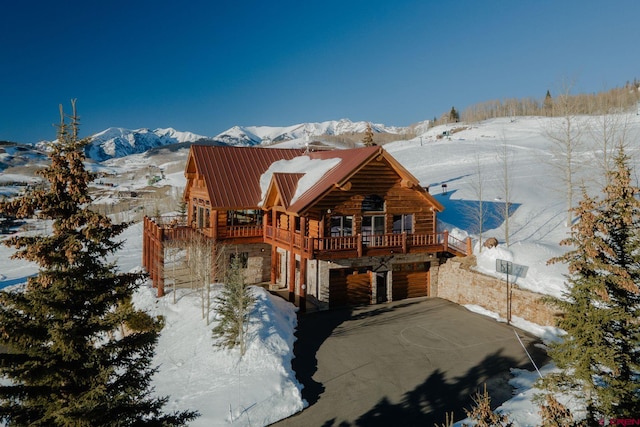 snow covered house featuring stone siding, a mountain view, and metal roof