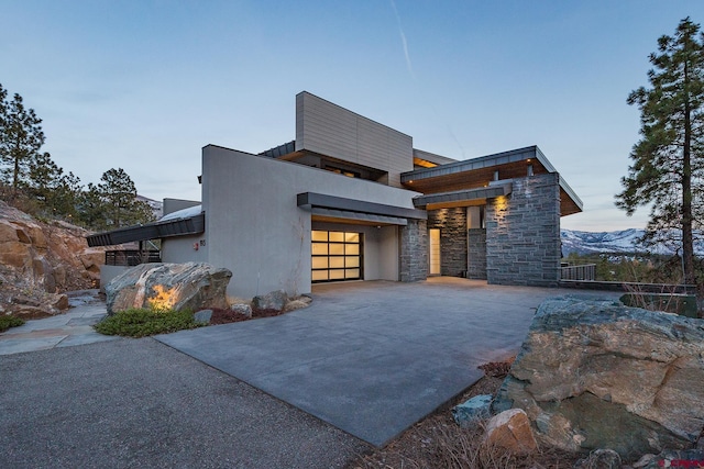 contemporary house featuring driveway, stone siding, a garage, and stucco siding