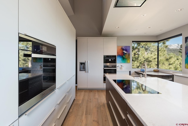 kitchen featuring a sink, white cabinets, light countertops, light wood finished floors, and modern cabinets