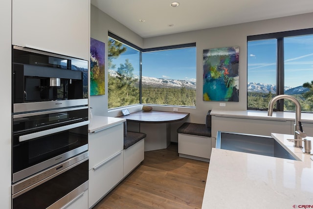 kitchen with breakfast area, modern cabinets, white cabinetry, a sink, and wood finished floors