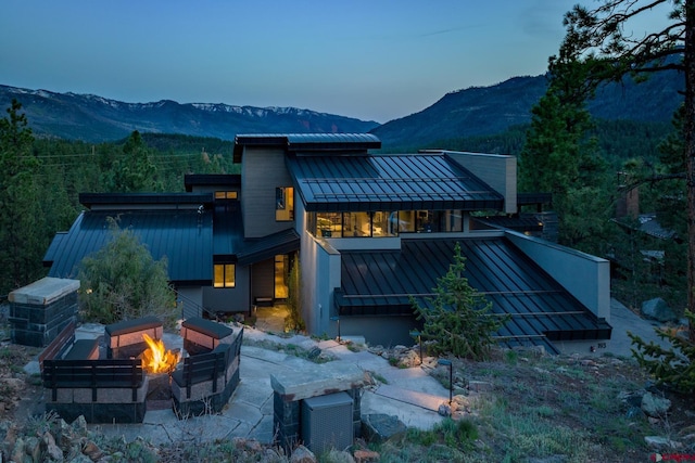 back of property featuring a standing seam roof, an outdoor fire pit, a mountain view, and metal roof