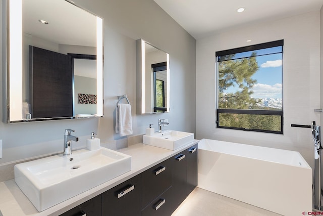 full bath with a freestanding bath, double vanity, a sink, and recessed lighting