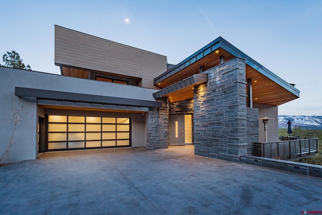 contemporary house featuring a garage, driveway, stone siding, a mountain view, and stucco siding