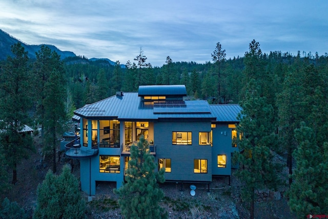 exterior space featuring a standing seam roof, metal roof, a view of trees, and roof mounted solar panels