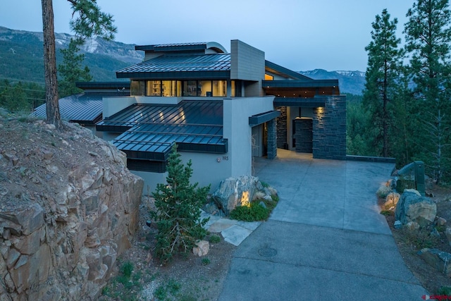 exterior space with a standing seam roof, a mountain view, metal roof, stone siding, and driveway