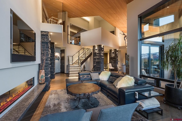 living room featuring a glass covered fireplace, wood finished floors, stairs, a high ceiling, and ornate columns