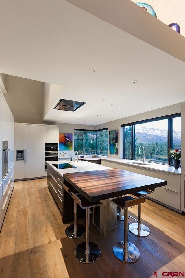 kitchen with light countertops, light wood-style flooring, white cabinets, a sink, and modern cabinets