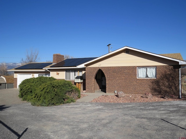 ranch-style house with a chimney, solar panels, and brick siding