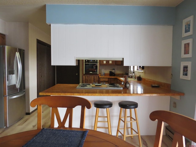 kitchen featuring light countertops, appliances with stainless steel finishes, white cabinets, a peninsula, and a kitchen bar