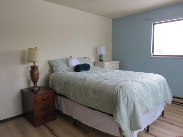 bedroom featuring light wood-type flooring, baseboards, and a textured ceiling