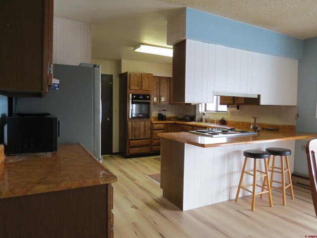 kitchen with a breakfast bar area, light wood-style flooring, a textured ceiling, a peninsula, and black appliances