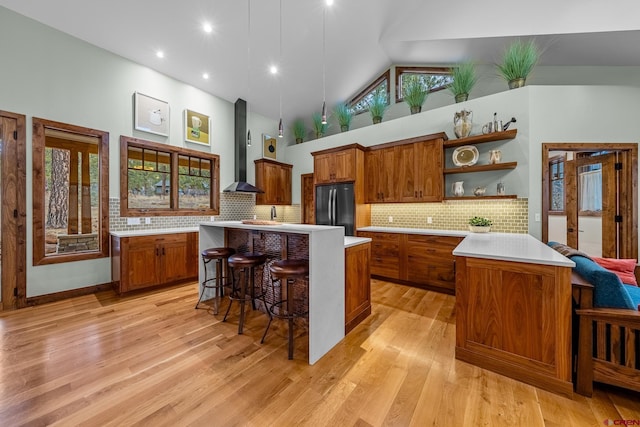 kitchen with refrigerator, open shelves, light countertops, brown cabinetry, and wall chimney range hood