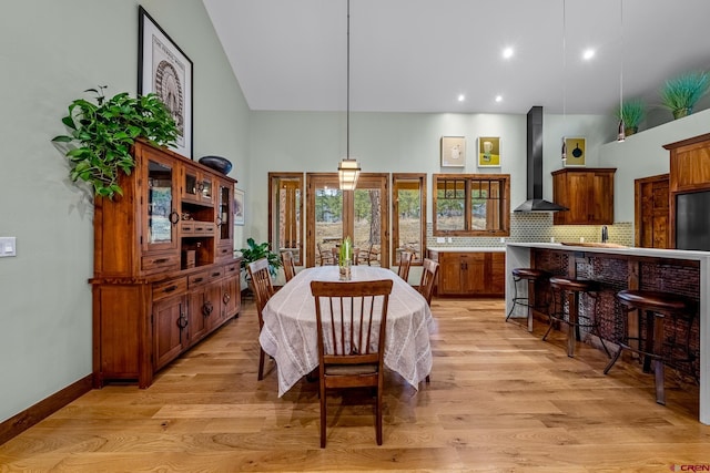 dining space with a towering ceiling, light wood-style flooring, and baseboards