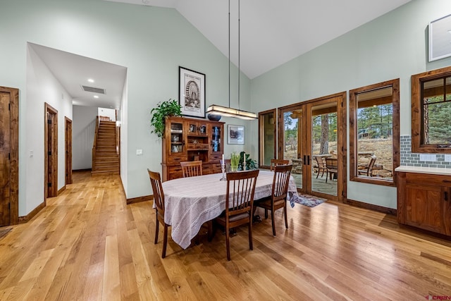 dining area featuring light wood finished floors, visible vents, stairway, high vaulted ceiling, and baseboards