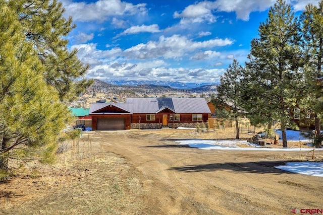 rustic home featuring driveway, stone siding, a garage, and metal roof