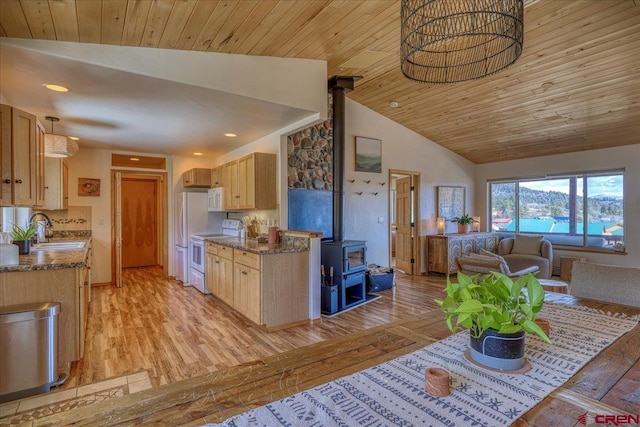 kitchen with light brown cabinets, white appliances, a sink, light wood finished floors, and a wood stove