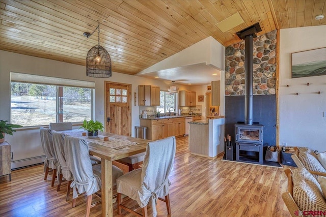 dining area with light wood finished floors, lofted ceiling, wooden ceiling, a baseboard radiator, and a wood stove