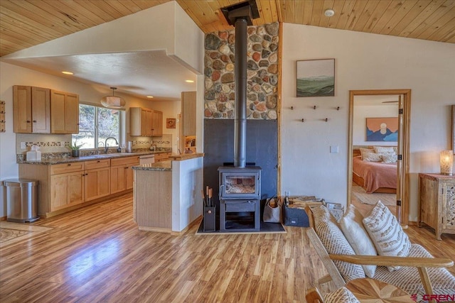 kitchen with vaulted ceiling, light wood-style flooring, a sink, and a wood stove