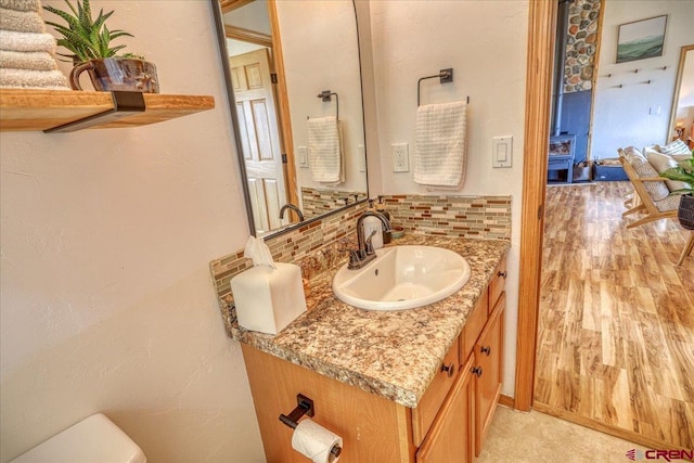 half bath with tasteful backsplash, vanity, toilet, and wood finished floors