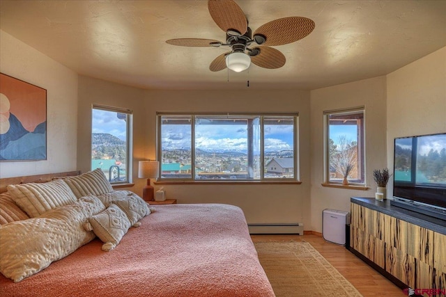 bedroom featuring light wood-type flooring, baseboard heating, and a ceiling fan