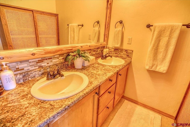 bathroom featuring baseboards, double vanity, a sink, and decorative backsplash