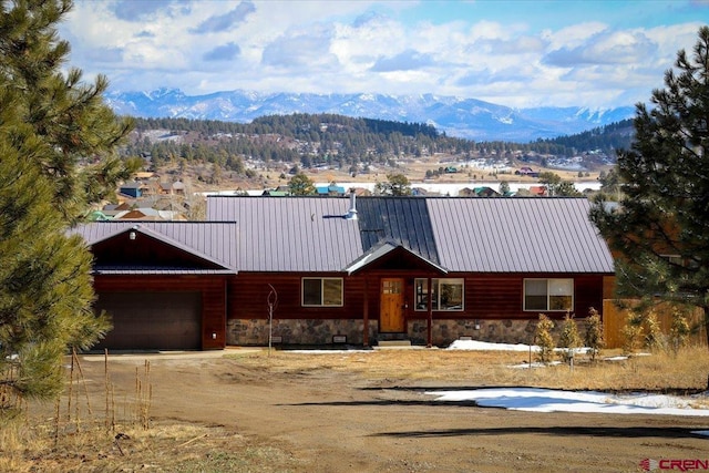 chalet / cabin with an attached garage, a mountain view, metal roof, stone siding, and driveway