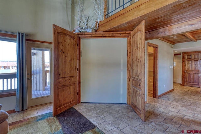 interior space with wooden ceiling, stone tile floors, a high ceiling, baseboards, and beamed ceiling