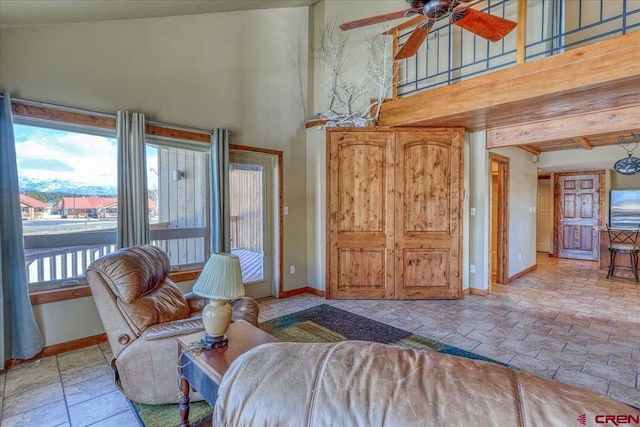 living area featuring stone tile flooring, ceiling fan, a towering ceiling, and baseboards