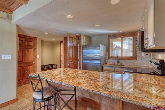 kitchen with stainless steel appliances, a sink, backsplash, and light stone counters