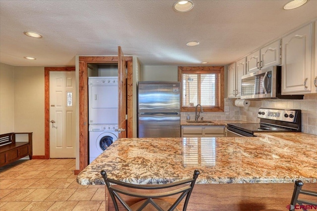 kitchen featuring stacked washer and dryer, tasteful backsplash, a peninsula, stainless steel appliances, and a sink