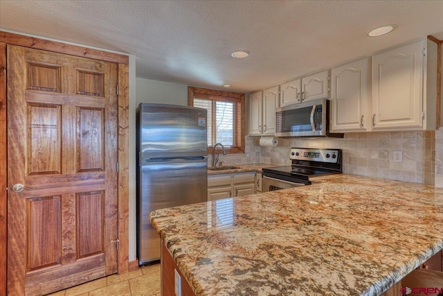 kitchen with a peninsula, a sink, white cabinets, appliances with stainless steel finishes, and tasteful backsplash