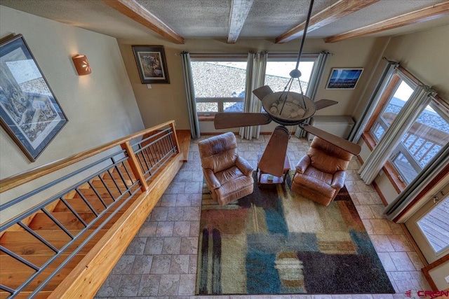 living room featuring a textured ceiling, baseboards, beam ceiling, and stone tile floors