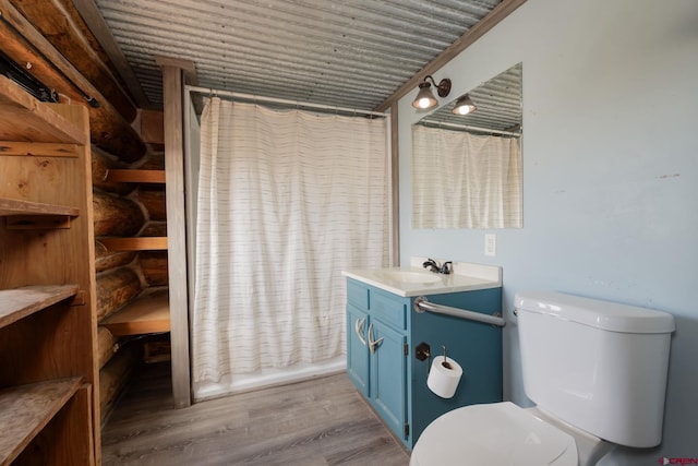 bathroom featuring toilet, rustic walls, wood finished floors, and vanity