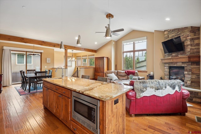 kitchen featuring stainless steel microwave, open floor plan, a kitchen island with sink, a fireplace, and a sink