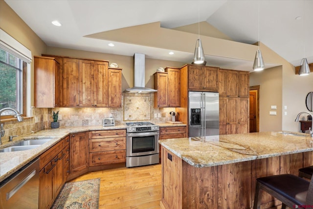 kitchen with stainless steel appliances, brown cabinetry, a sink, and wall chimney exhaust hood