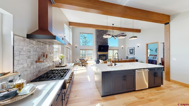 kitchen with a fireplace, stainless steel appliances, open floor plan, a sink, and wall chimney range hood