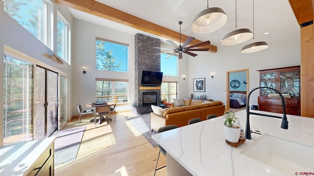 interior space featuring a large fireplace, a ceiling fan, a towering ceiling, light wood-style floors, and beam ceiling