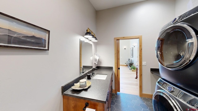 laundry area featuring dark tile patterned flooring, cabinet space, a sink, and stacked washing maching and dryer