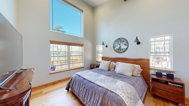 bedroom with a towering ceiling, multiple windows, baseboards, and wood finished floors