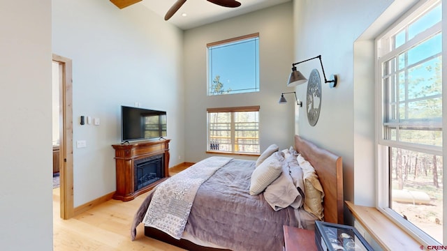 bedroom with light wood-style floors, multiple windows, a high ceiling, and a fireplace