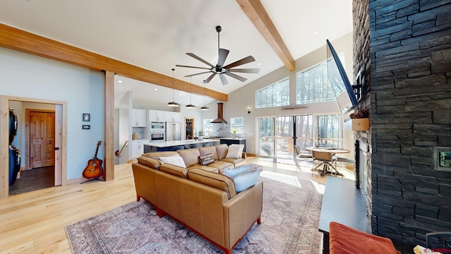 living room with high vaulted ceiling, a stone fireplace, a ceiling fan, beam ceiling, and light wood finished floors