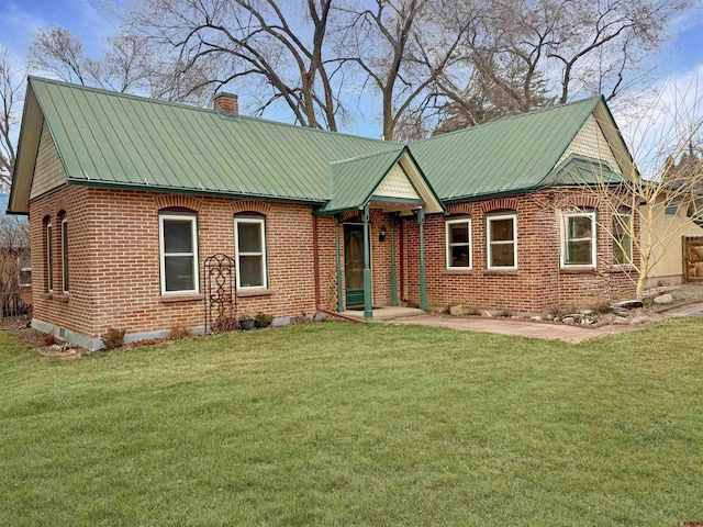 view of front of property featuring metal roof, a front lawn, a chimney, and brick siding