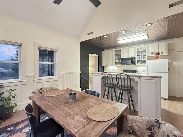 dining room featuring a wainscoted wall, vaulted ceiling, arched walkways, and visible vents