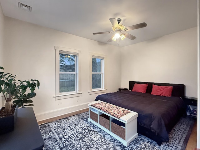 bedroom with a ceiling fan, wood finished floors, visible vents, and baseboards