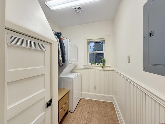 clothes washing area featuring a wainscoted wall, stacked washer and dryer, light wood-style floors, laundry area, and electric panel