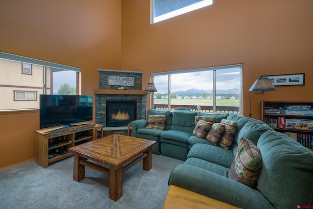 carpeted living room featuring a healthy amount of sunlight, a towering ceiling, and a stone fireplace