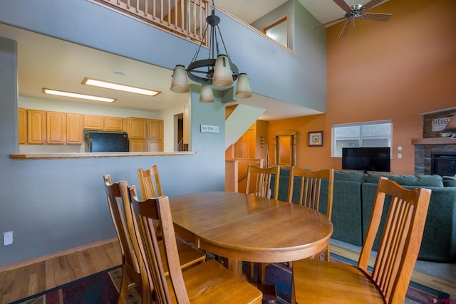 dining area featuring a fireplace, wood finished floors, a towering ceiling, and a ceiling fan